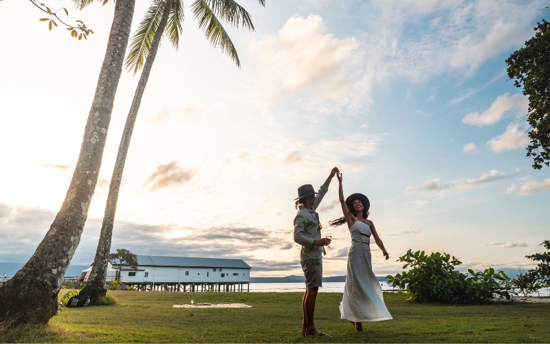 Couple dancing beneath palm trees in Port Douglas with sunset skies and the historic Sugar Wharf visible in the background overlooking the waterfront.