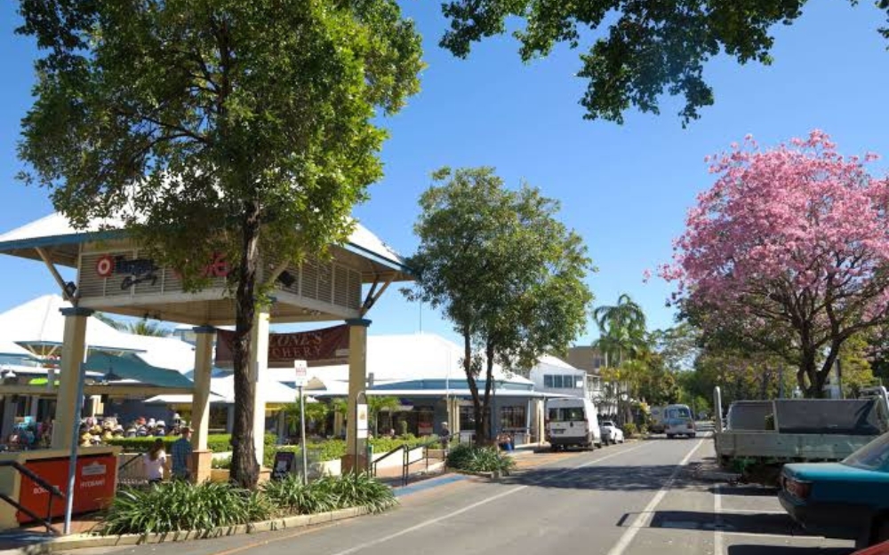 Entrance to Port Village Shopping Centre in Port Douglas, surrounded by tropical landscaping, shops and outdoor dining areas.