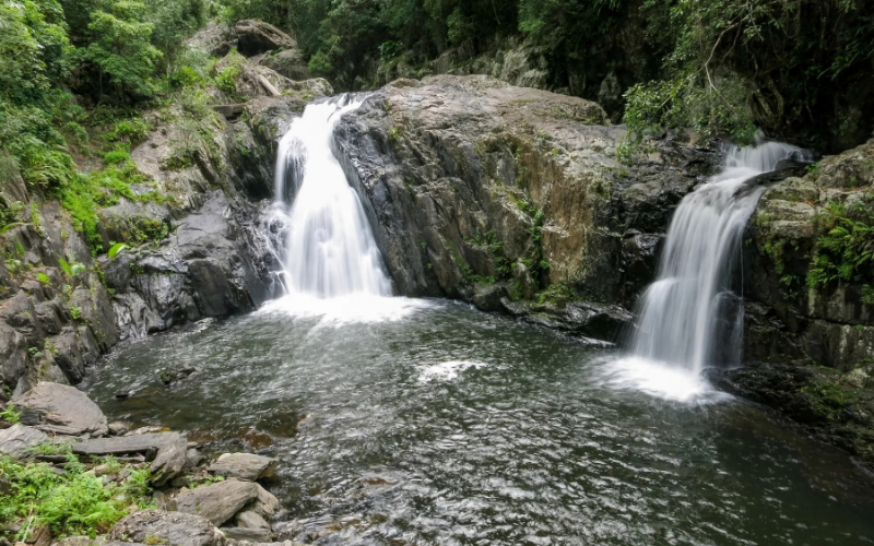 Twin waterfalls flowing over rocky ledges into a natural swimming pool at Crystal Cascades near Cairns.