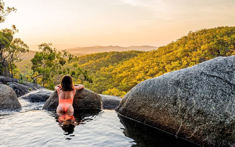 Swimmer enjoying a natural rock pool at Davies Creek Falls with sweeping views across the forested Atherton Tablelands.